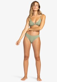 Bikini set v mátově zelené barvě, který se vyznačuje strukturální látkou, trojúhelníkovým topem s detailem středového uzlu a nízkými bikinovými kalhotkami.