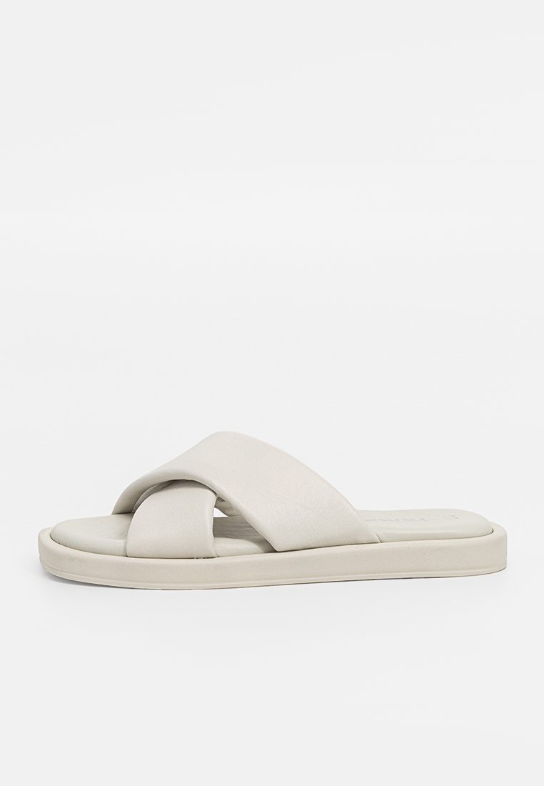 Beige Rutsch-Sandale aus weichem Leder, mit einem Kreuzriemen-Design und einer flachen Gummisohle, glatter Textur und minimalistischem Stil.