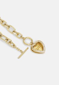 Collier en chaîne doré avec un pendentif en forme de cœur au intérieur texturé, entouré de strass transparents, et avec un fermoir à bascule.