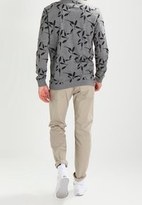 Sweat-shirt gris avec motif de feuilles, pantalon beige et baskets blanches ; il présente des manches longues, un col rond et une coupe décontractée.