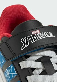 Svart och blå sneaker med Spider-Man-design, röd nätkrage, vita snören och logopatch på ett band. Spindelnätmönster synligt.