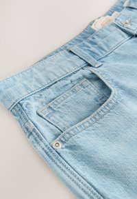 Jeans in denim azzurro chiaro, con una cintura standard, una tasca frontale e dettagli di cuciture visibili, con una texture liscia e leggermente consumata.