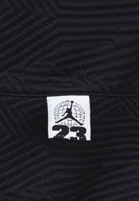 Tissu noir avec un motif en zigzag texturé, affichant une étiquette blanche avec la silhouette d'un joueur de basketball sur le chiffre "23" et un fond de globe.