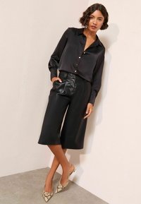 Sort satin skjorte med lange ærmer og knapper, parret med højtaljede faux læder culottes og teksturerede slangeskinds slingback hæle.