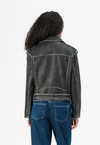 Black faux leather jacket with white stitching details, wide collar, and structured seams, paired with blue high-waisted jeans.