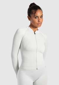 Hvid zip-up langærmet top med ribbet tekstur og høj krave. Har en frontlynlås og tilpasset design, som er parret med matchende underdele.