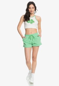 Haut court blanc avec un motif de feuilles vertes, associé à un short à cordon de serrage vert clair. Il présente une coupe décontractée et une texture de tissu douce.