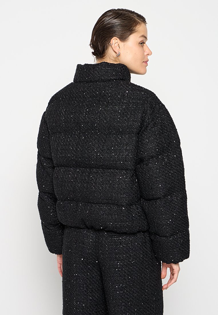 Schwarze Daunenjacke mit strukturiertem Oberflächenmaterial und glitzernden Akzenten. Hoher Kragen und lockerer, gepolsterter Schnitt. Geeignet für kaltes Wetter.