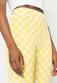Leggings amarelas com um padrão repetido de corações brancos, textura canelada e um design justo, combinadas com um top branco cropped.