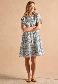 Šaty s kvetinovým vzorom, krátkymi rukávmi, okrúhlym výstrihom a zhromaždeným pásom. Farby zahŕňajú bielu, modrú a zelenú. Nosia sa s žltými sandálmi.