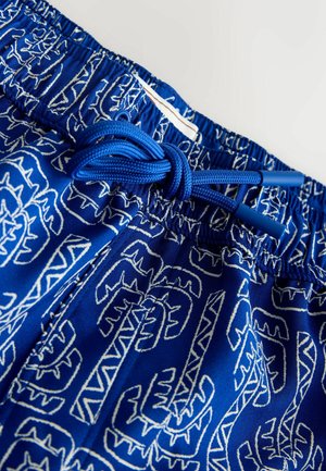 Mėlyni šortai su elastine juosmens juosta, mėlyna raišteliu ir baltais abstrakčiais geometriniais raštais audinyje.