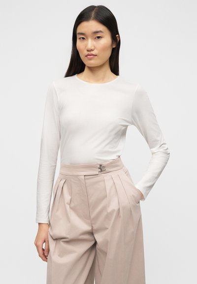 Μπλούζα με μακριά μανίκια σε ανοιχτό μπεζ χρώμα με απαλή υφή, σε συνδυασμό με ψηλόμεσα, απαλό ροζ παντελόνια με πιέτες και μεταλλικό κούμπωμα.