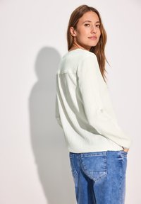 Lys grøn, struktureret bluse med lange ærmer og rund halsudskæring, parret med blå denim jeans, set bagfra.