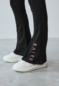 Sorte bukser med en flared design, med "BAKER" i farverige bogstaver på siden. Parret med hvide, teksturerede sneakers.