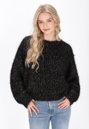 Zwarte vachtachtige trui met kleurrijke stippen, ronde halslijn, losse pasvorm en lange mouwen, gecombineerd met lichtblauwe jeans. Zachte textuur zichtbaar.