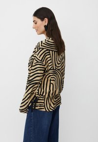 Blusa beige con linee astratte nere, maniche lunghe, vita con cordoncino e vestibilità rilassata, abbinata a jeans a gamba larga blu scuro.