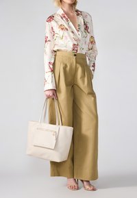 Langærmet bluse med blomsterprint i creme, højtaljede khaki-bukser og en struktureret beige tote-bag med lynlås og lange hanke.