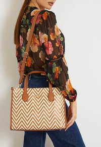Struktureret beige og hvid chevron-mønstrede taske med brune remme og kanter, der har dobbelte top-håndtag og en aftagelig skulderrem.