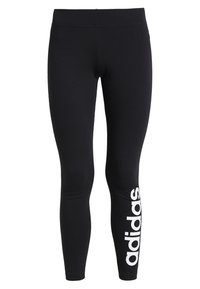 Czarne legginsy wykonane z elastycznej tkaniny o gładkiej fakturze. Posiadają dużą białą grafikę z logo "adidas" wydrukowaną pionowo na lewym udzie.