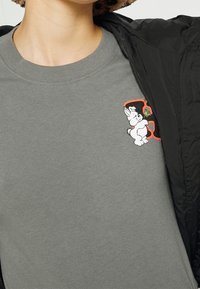 Heather-graues Baumwoll-T-Shirt mit einem kleinen bestickten weißen Hasenmotiv mit bunten Akzenten auf der linken Brust.