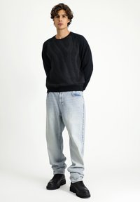 Felpa nera con motivo testurizzato, maniche lunghe, abbinata a jeans di denim azzurro chiaro e scarpe nere chunky.