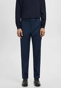 Granatowe, dopasowane spodnie o prostym kroju, z płaskim przodem, szlufkami na pasek i gładką fakturą, zestawione z czarnymi butami.