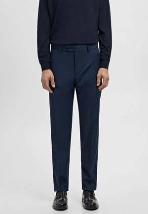 Marineblaue, maßgeschneiderte Hose mit geradem Schnitt, flacher Vorderseite, Gürtelschlaufen und glatter Textur, kombiniert mit schwarzen Schuhen.