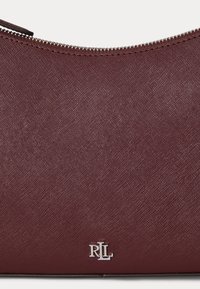 Primo piano di un astuccio in pelle bordeaux testurizzata con una cerniera argento e un piccolo logo RLL argento vicino al centro in basso.