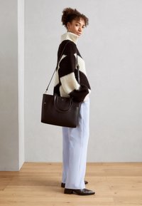 Sort læder tote bag med runde håndtag, tekstureret finish og en aftagelig skulderrem, parret med en hyggelig sort og hvid sweater.