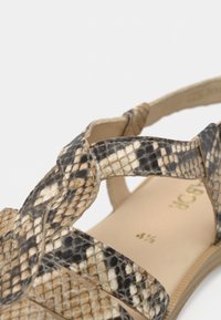 Πέδιλο με λουράκια που διαθέτει υφή δέρματος φιδιού σε αποχρώσεις του μαύρου και του μπεζ, με ομαλή μπεζ εσωτερική σόλα και ουδέτερη σόλα από καουτσούκ.