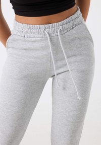 Pantalones de chándal grises con cinturilla elástica, cordón ajustable y una textura suave. El diseño cuenta con bolsillos laterales y un ajuste relajado.