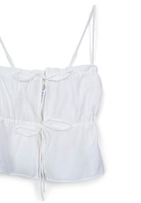 Top corto bianco realizzato in tessuto morbido, caratterizzato da spalline sottili regolabili, una vita cinchata e un dettaglio con nodo al centro davanti.