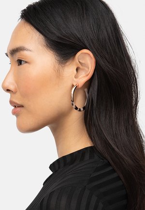 Gouden hoepeloorbel met een schildpadpatroon en een gladde oppervlakte. Het ontwerp heeft een dunne, open stijl voor lichtgewicht draagcomfort.