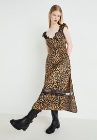 Robe à imprimé léopard avec un passepoil en dentelle, des manches courtes et une fente latérale. Portée avec des bottes à talons noires avec des boucles.
