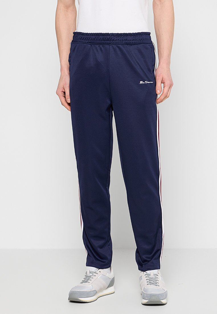 Marineblauwe sportbroek met een trekkoord in de taille, voorzien van witte en rode zijstrepen en een gladde, lichte stof.