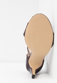 Chaussure à talon de couleur violet foncé, avec une texture gaufrée crocodile, un bout pointu et un talon aiguille fin. La semelle est lisse et de couleur beige.