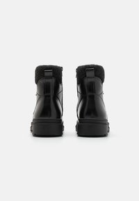 Botas de cuero negro con cuellos de fieltro gris, punta redonda y suelas de goma. Presentan una pestaña en la parte posterior y detalles de costura limpios.