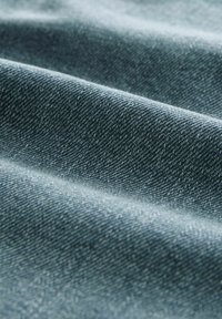 Material denim într-o nuanță albastru mediu, având o textură țesută cu cusături vizibile, evidențiind pliuri și cute pentru adâncime.