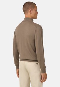 Pruun kootud sviiter kõrge kraega, kitsas lõige ja soonikuga mansetid. Kanda heledate pükste, minimaalsete disaini ja ilma silmapaistvate mustriteta.