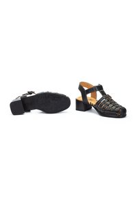 Sandalias de cuero negro con diseño de punta cerrada y cortes, correa ajustable y tacón cuadrado, con una suela de goma texturizada.