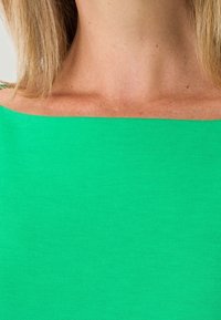 Zielona bluzka odkrywająca ramiona, wykonana z miękkiego, elastycznego materiału; gładka tekstura, jednolity kolor i minimalistyczny design.
