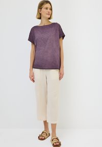 Lilla blød T-shirt med korte ærmer, forsynet med skulderknapper, parret med cremede bredbenede teksturerede bukser og flettede sandaler.