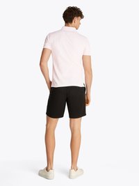 Camisa polo rosa clara com mangas curtas, combinada com calções pretos e sapatilhas de cor clara, vista de trás. Textura de tecido suave.
