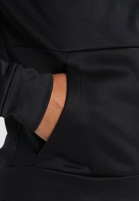 Sudadera negra con un bolsillo lateral y una textura suave; puños ajustados en una tela elástica.