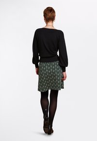 Schwarzer Langarm-Pullover mit weitem Ausschnitt, kombiniert mit einem grünen gemusterten Rock mit cremefarbenen Blumenmotiven und einem ausgestellten Saum.