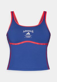 Blå atletisk crop top med röda detaljer och remmar. Har "ADIDAS TRAINING CLUB"-logotypen i vitt i mitten. Slät, tight passform.