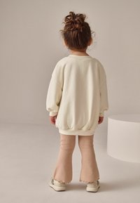 Lys creme oversized sweatshirt med puffede ærmer, parret med lys pink ribbede flared bukser. Skoene har et tekstureret mønster.