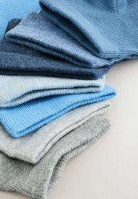 Stapeltje opgevouwen wollen truien in verschillende tinten blauw en grijs op een lichte ondergrond, met zichtbare zachte breistructuren.