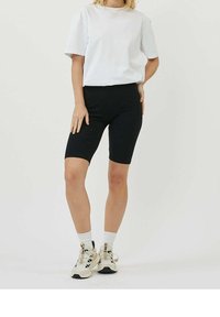 Un short de vélo noir en tissu extensible, associé à un t-shirt blanc ample. Porté avec des baskets de couleur claire et des chaussettes à la cheville.