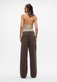 Καφέ παντελόνι με φαρδύ κόψιμο και ψηλή μέση, άνετη εφαρμογή, και δύο πίσω τσέπες, συνδυασμένο με ένα εφαρμοστό λαμπερό χρυσό τοπ.